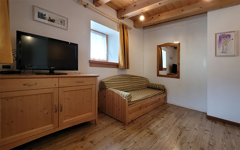 Gemütliches Wohnzimmer in einem Apartment des Chalet Royal in Arabba, mit Schlafsofa, TV und Holzmöbeln.