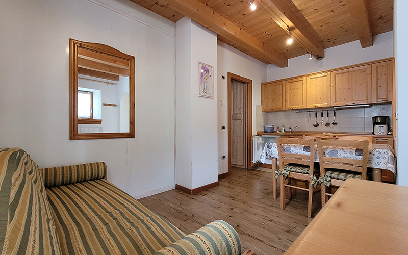 Innenansicht eines Chalet Royal Apartments in Arabba: Wohnzimmer mit gestreiftem Sofa und ausgestatteter Holzküche.