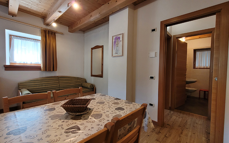 Innenansicht eines Chalet Royal Apartments in Arabba mit Esstisch, Sofa und Zugang zum Badezimmer.
