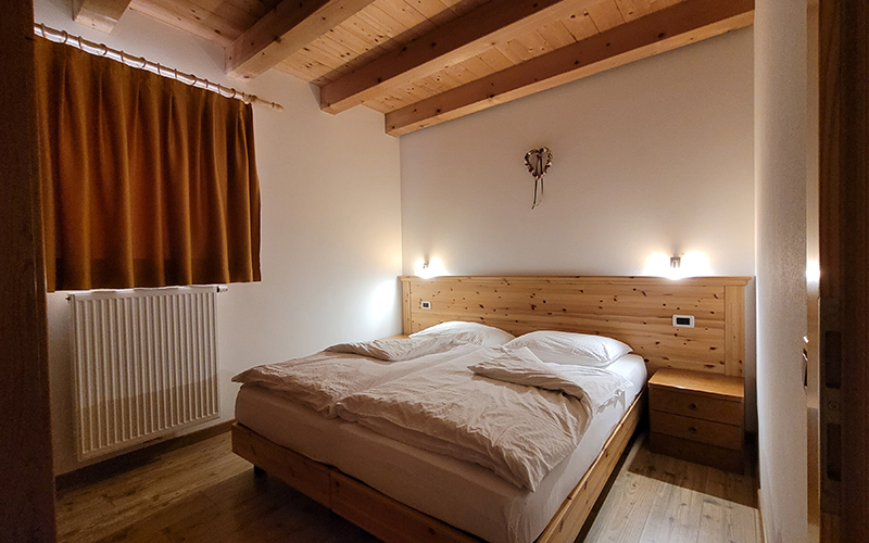 Gemütliches Doppelzimmer im Chalet Royal in Arabba, mit Holzbetten, Balkendecke und Blick auf die Dolomiten.