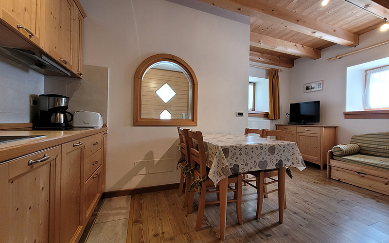 Küche und Essbereich eines Chalet Royal Apartments in Arabba, mit hellen Holzmöbeln und sichtbaren Balken.