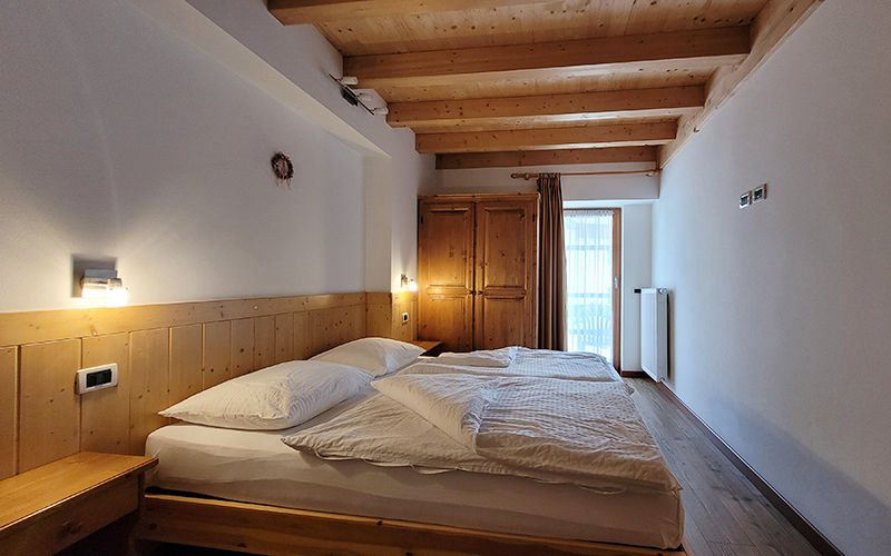 Helles Doppelbett aus Holz im Chalet Royal in Arabba, mit sichtbaren Deckenbalken.