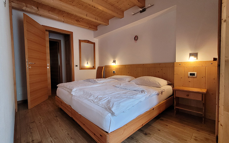 Helles Doppelbett aus Holz mit Sichtbalken, Bett mit weißen Laken und Nachttisch.