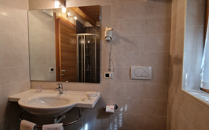 Modernes und helles Badezimmer eines Chalet Royal Apartments in Arabba, mit Waschbecken, Spiegel und Dusche.