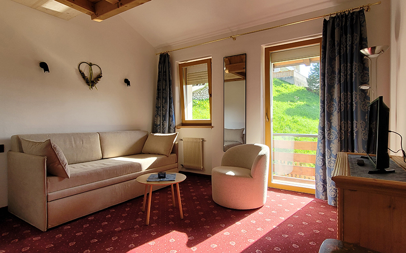 Geräumige Suite im Garni Royal in Arabba mit Schlafsofa, Sessel, TV und Balkon mit Dolomitenblick.