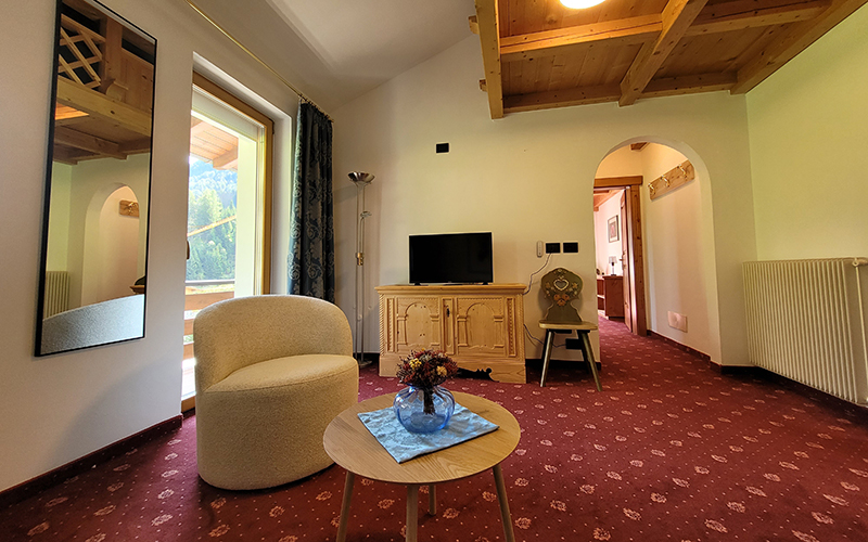 Suite des Garni Royal in Arabba mit Sessel, Beistelltisch, TV auf Holzmöbel und Blick auf die Dolomiten.