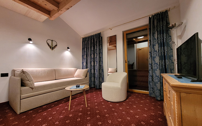 Geräumige Suite im Garni Royal in Arabba mit Schlafsofa, Sessel, rotem Teppich und Balkonzugang.