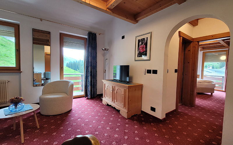 Geräumige Suite im Garni Royal in Arabba mit rotem Teppichboden, Balkon mit Dolomitenblick und Holzmöbeln.