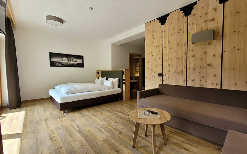 Suite des Garni Royal in Arabba mit Doppelbett, Sofa, Holzboden und Zirbenholzwand.