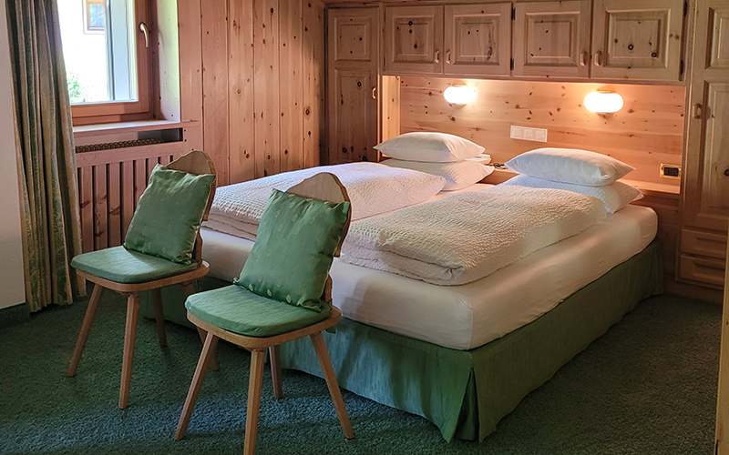 Doppelzimmer des Garni Royal in Arabba, mit Einzelbetten, Zirbenholzmöbeln und grünen Sesseln.