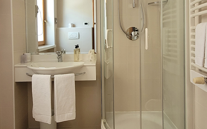 Modernes, helles Badezimmer im Garni Royal mit Waschbecken, Spiegel, Dusche und Handtuchheizkörper mit Handtüchern.