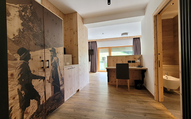 Geräumige Zirbenholz-Suite im Garni Royal in Arabba, mit Doppelbett, Schreibtisch und Balkon mit Dolomitenblick.