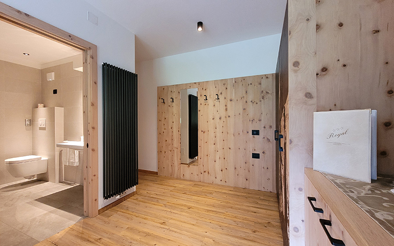 Zirbenholzkorridor mit Spiegel, Garderobe und Zugang zu einem modernen Badezimmer, typisch für die Zimmer des Garni Royal in Arabba.