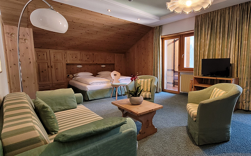 Zirbenholz-Suite im Garni Royal in Arabba mit Einzelbetten, Sofa, Sesseln und Balkon.