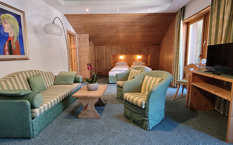 Suite des Garni Royal in Arabba mit Sofa, Sesseln, Einzelbetten und Zirbenholzmöbeln.
