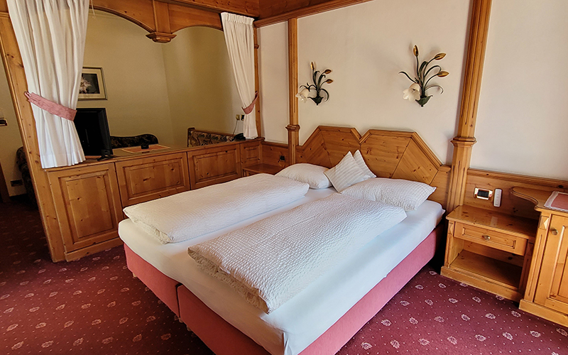 Doppelzimmer des Garni Royal in Arabba, mit Kingsize-Bett, Zirbenholzmöbeln und rotem Teppich.