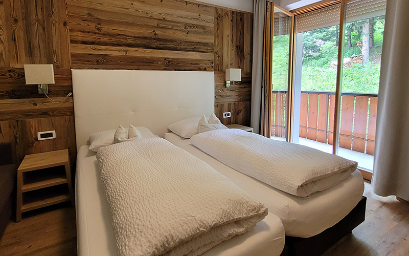 Doppelzimmer im Garni Royal in Arabba, mit Zirbenholzwänden, Einzelbetten und Balkon mit Blick auf die Dolomiten.