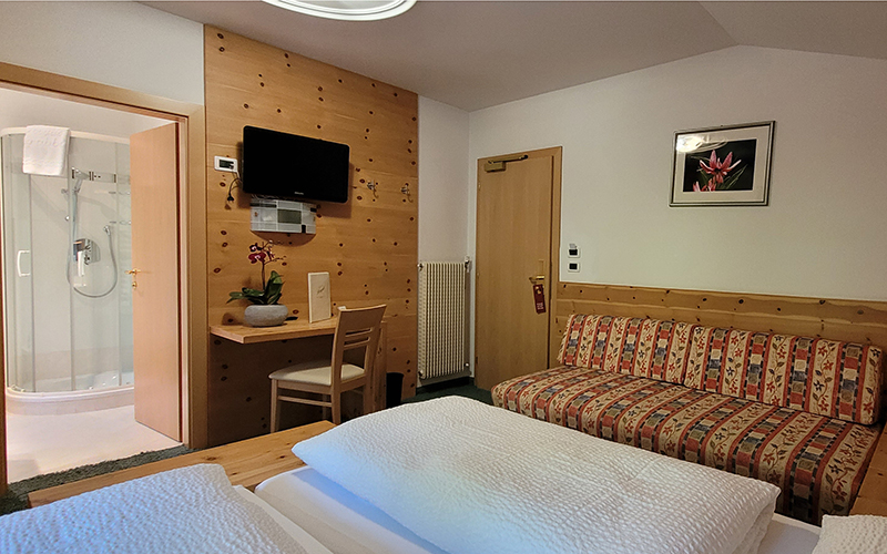 Helles Doppelbett aus Holz mit Sichtbalken, Bett mit weißen Laken und Nachttisch.