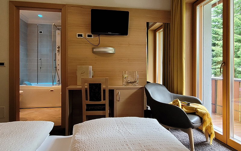 Zirbenholz-Suite im Garni Royal in Arabba mit Bett, Schreibtisch, Sessel, TV und Bad mit Whirlpool-Badewanne.