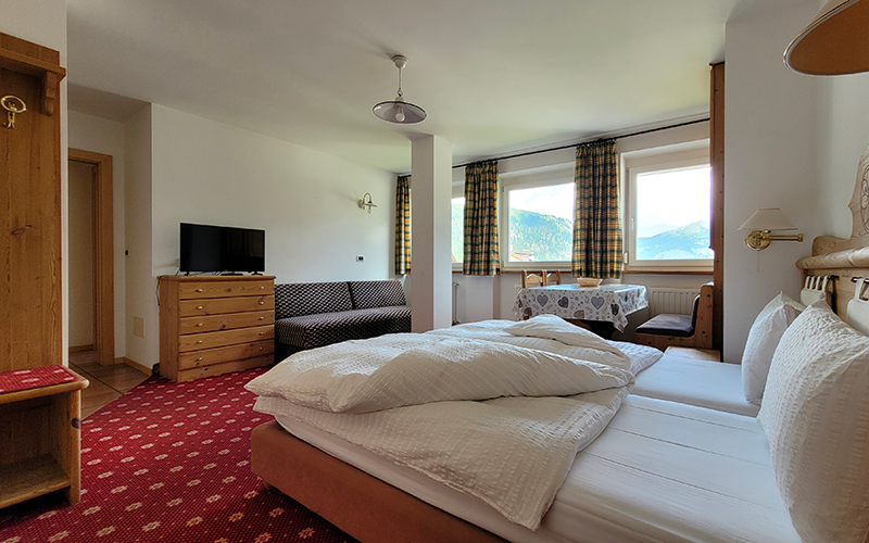 Alpenroyal apartment in mountain style with a double bed, sofa, TV, and table with a view of the Dolomites.
