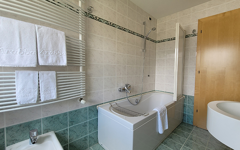 Modern and bright bathroom of an Alpenroyal apartment in Arabba, with bathtub, shower, and heated towel rail.