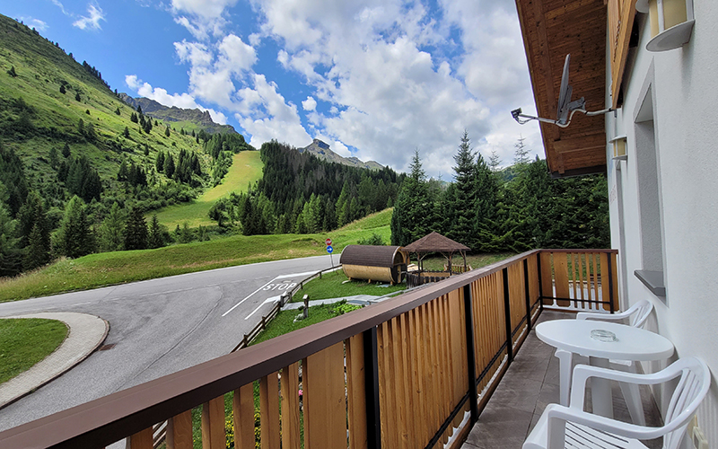 Balcony of the Alpenroyal Apartment with table and chairs, view of the street, barrel sauna, and Dolomites.