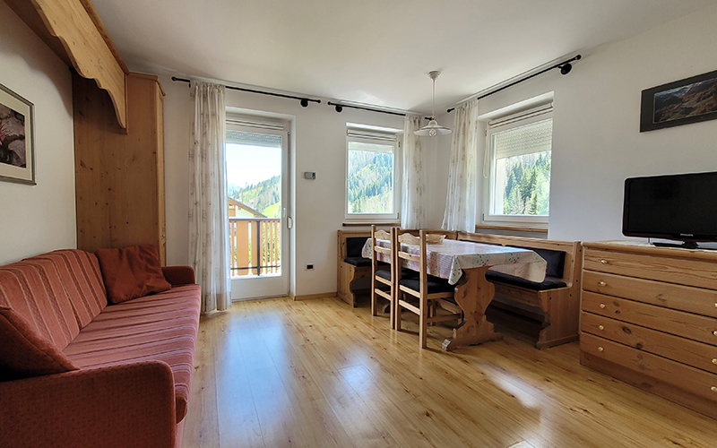Alpenroyal apartment in Arabba: living room with sofa, wooden dining table, and view of the Dolomites.