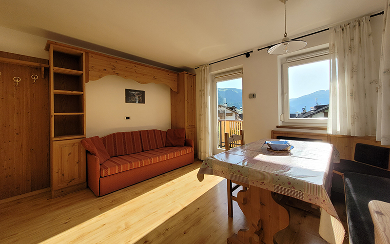 Spacious living room of an Alpenroyal apartment with a sofa bed, dining table, and view of the Dolomites.