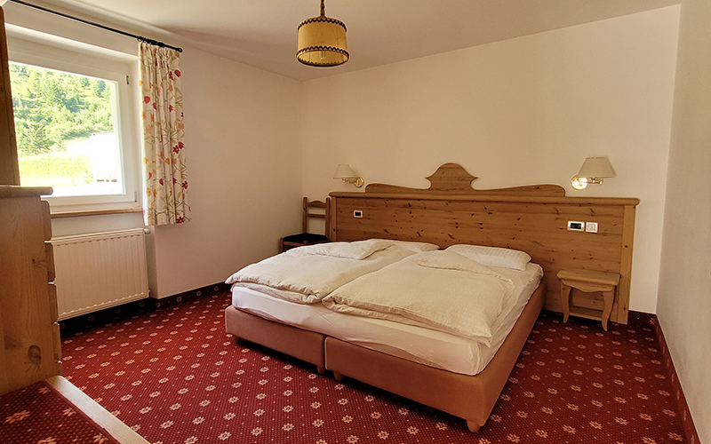 Mountain-style double bedroom with bed, wooden headboard, nightstands, and red carpet.