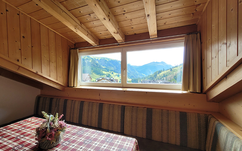 Alpenroyal apartment in mountain style with a double bed, sofa, TV, and table with a view of the Dolomites.