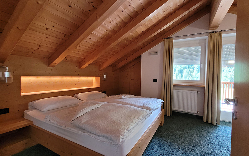 Light wooden double bedroom with exposed beams, bed with white sheets, and a nightstand.