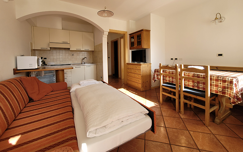 Alpenroyal apartment in Arabba: studio apartment with equipped kitchenette, sofa bed, and dining table.