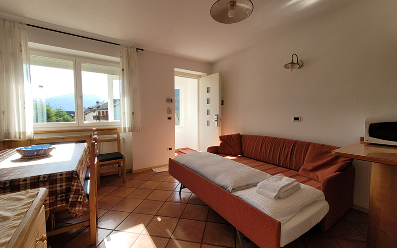 Alpenroyal apartment in Arabba: living room with sofa bed, dining table, and view of the Dolomites.