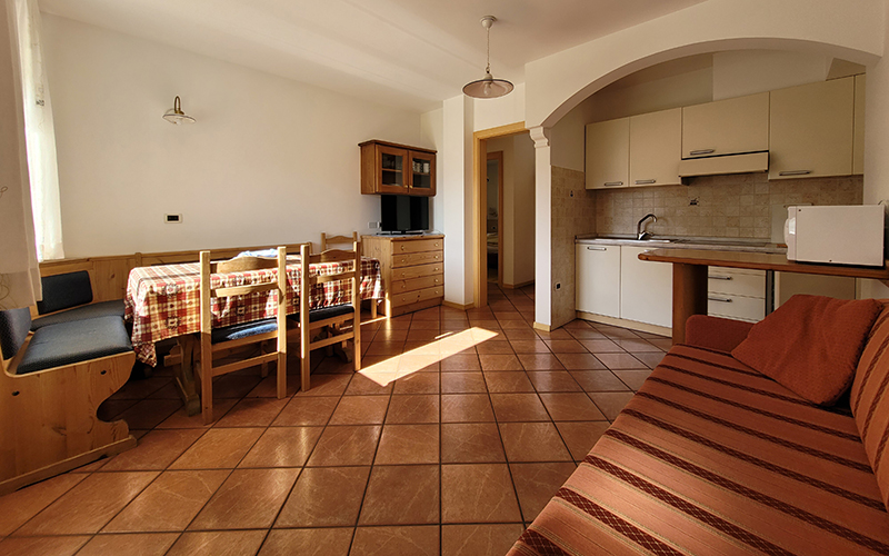 Alpenroyal apartment in Arabba: living room with wooden dining table, sofa, and equipped kitchen.
