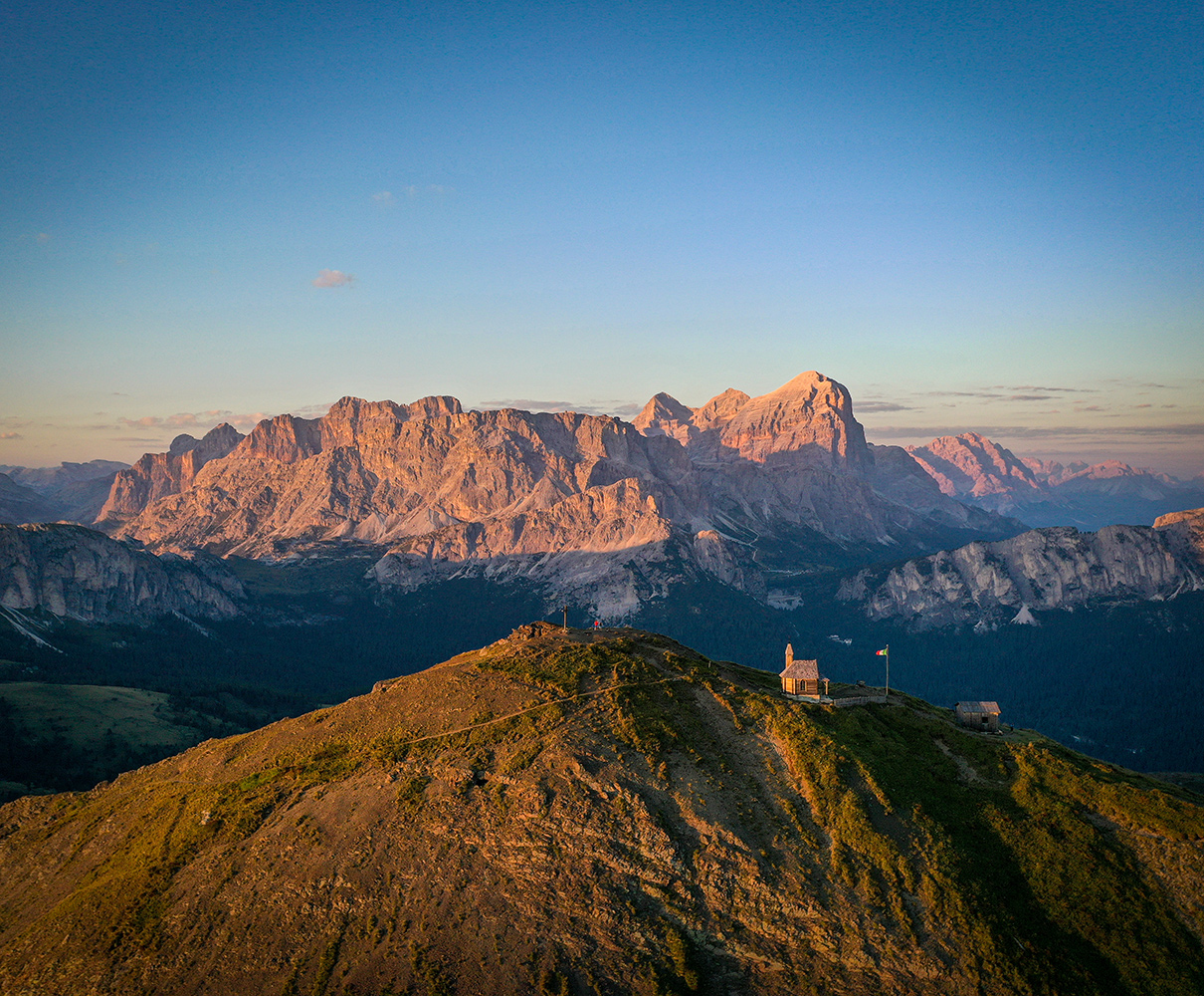 Panoramic view of the Dolomites at sunset with a small church and a mountain hut on a ridge, ideal for holidays in Arabba.