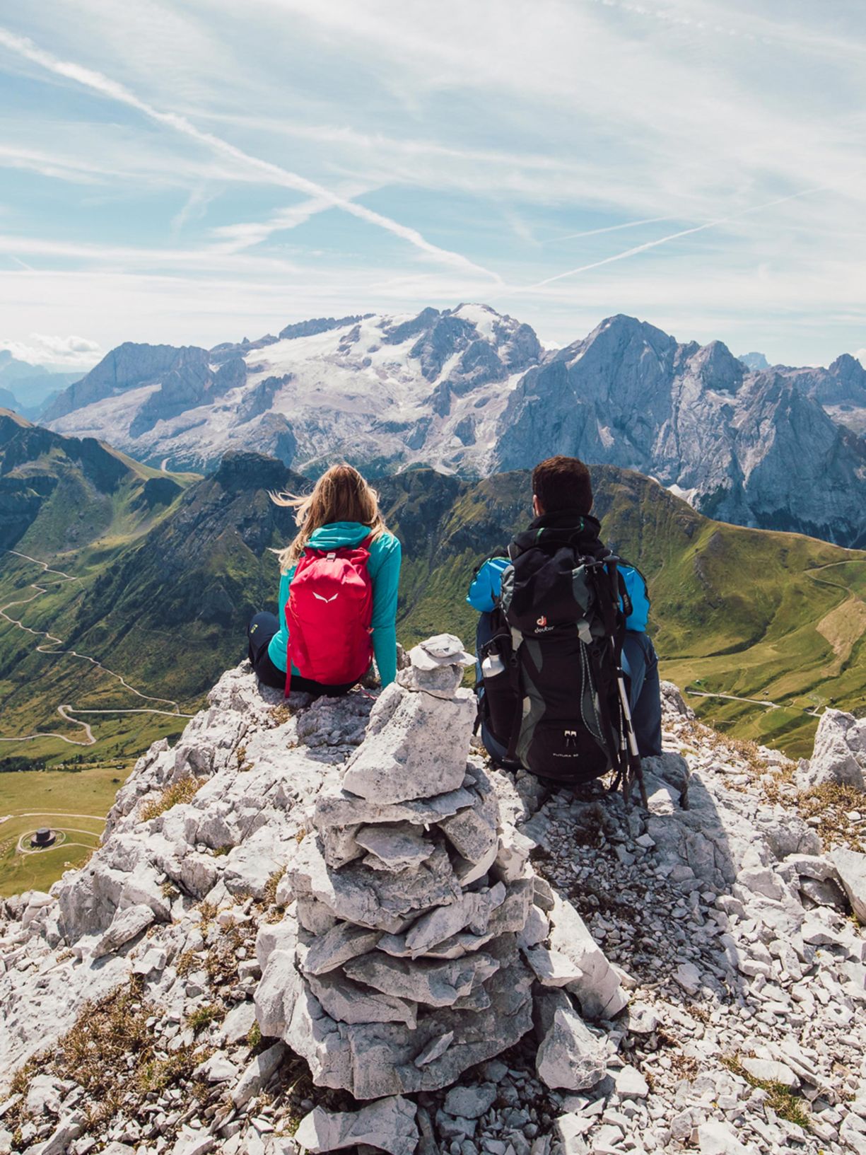 Two hikers with backpacks admire the snow-covered Dolomites from a rocky peak in Arabba.