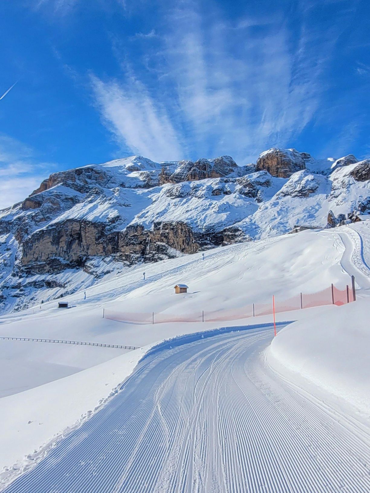 A perfectly groomed ski slope in Arabba, with the majestic snow-covered Dolomites and a blue sky.