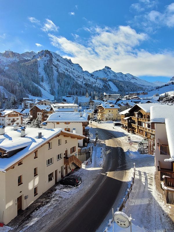 Panoramablick auf Arabba im Winter, mit verschneiten Häusern und Hotels und den majestätischen Dolomiten unter blauem Himmel.