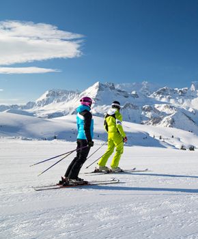 Two skiers in colorful attire admire the snow-covered Dolomites of Arabba, perfect for a ski holiday.