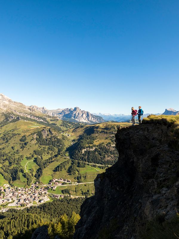 Due escursionisti ammirano il panorama mozzafiato delle Dolomiti e della valle di Arabba da un dirupo.
