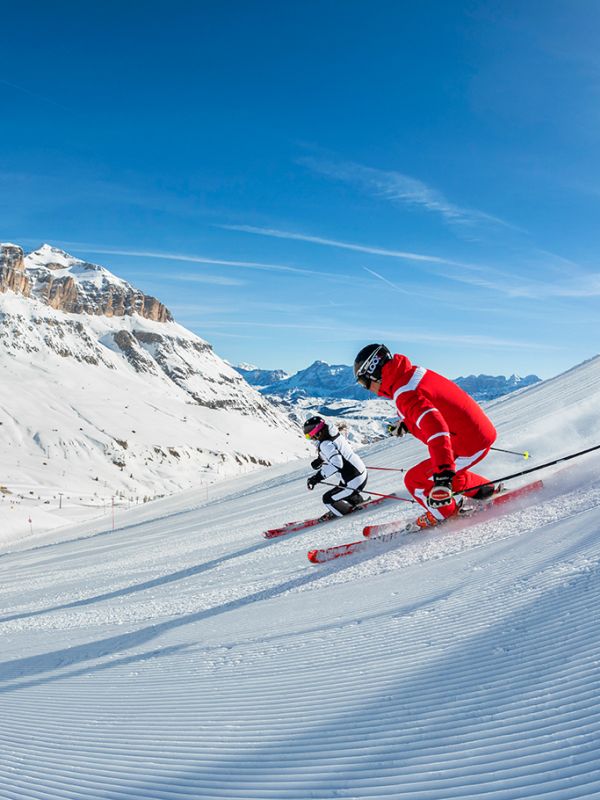 Due sciatori in tuta rossa e bianca scendono una pista perfettamente battuta ad Arabba, Dolomiti.