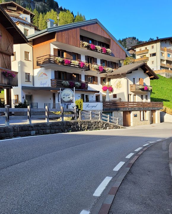 Facade of Garni Royal in Arabba, with flowered balconies and a sign, nestled in the Dolomites.