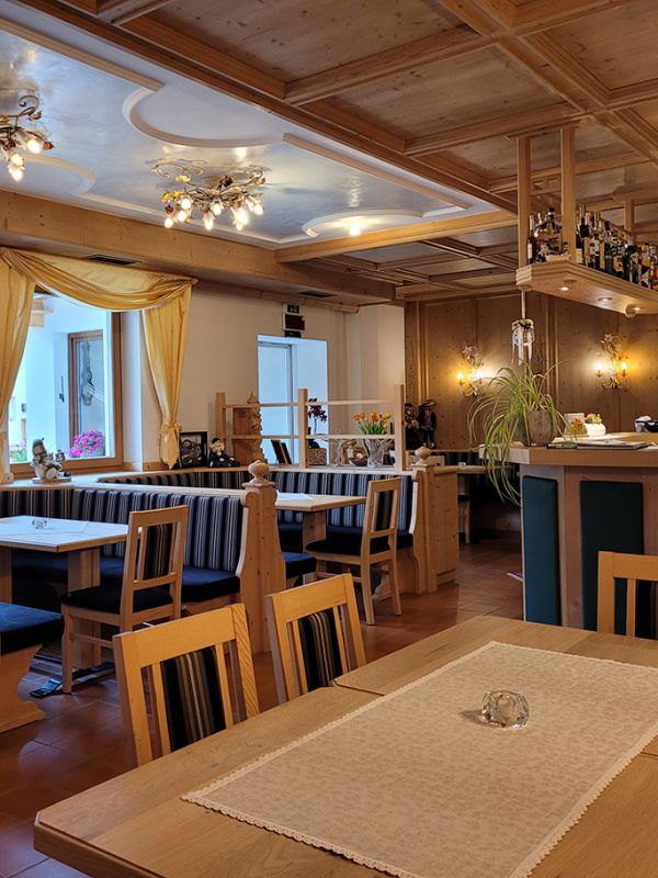 Innenansicht der Bar des Garni Royal in Arabba, mit Holztischen, gepolsterten Bänken und einer gut ausgestatteten Theke.