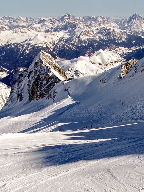 Wide panoramic view of the snow-covered Dolomites of Arabba, with skiers on the slopes and the Marmolada on the horizon.