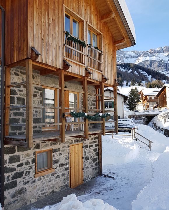 The Chalet Royal in Arabba, with wooden balconies and stone walls, nestled in the snow of the Dolomites.